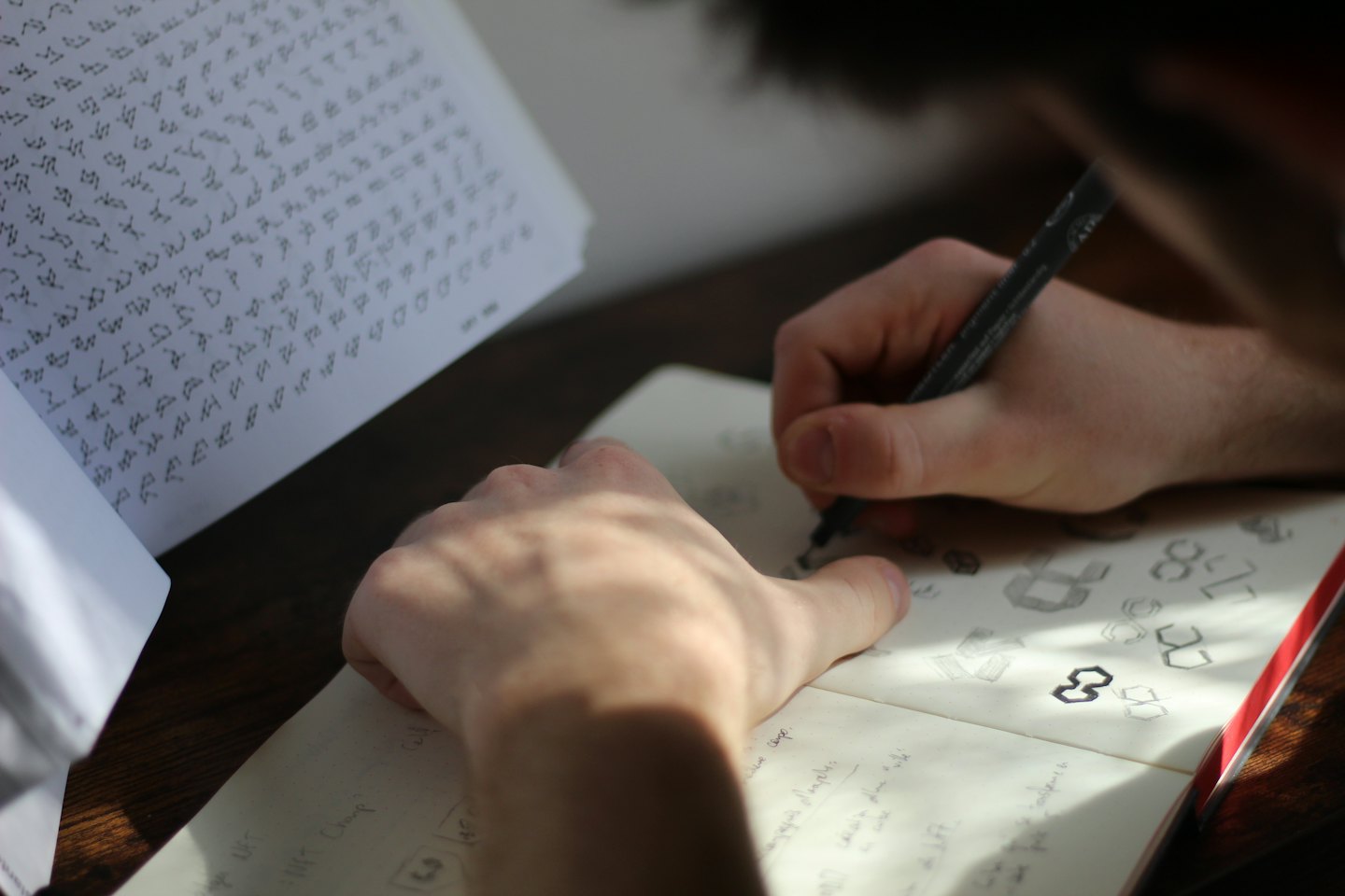 Mani che disegnano bozzetti di loghi su un taccuino con una penna.